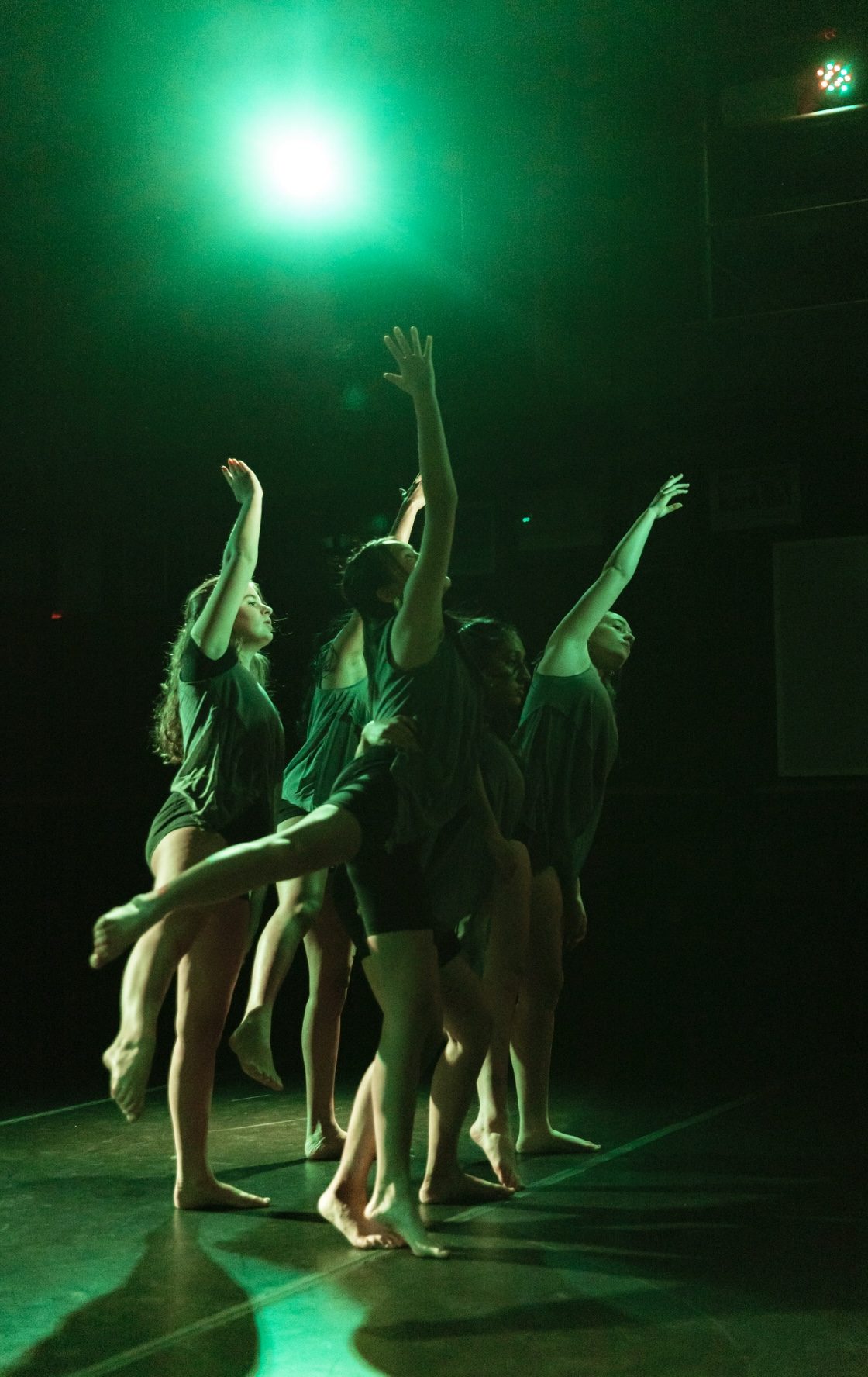 The dance company reaching upward under green light