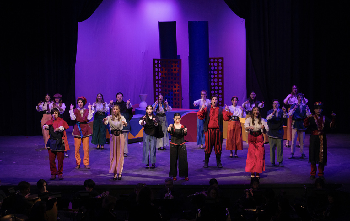 The full ensemble on stage under purple light