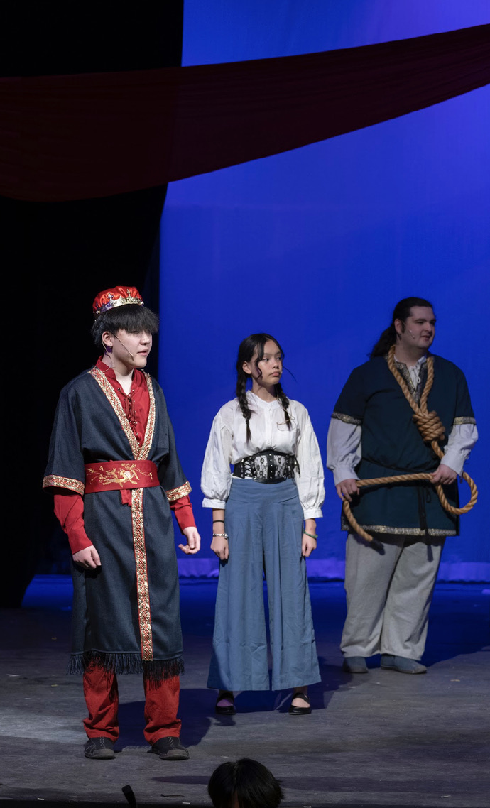 Bella on stage in costume between two castmates